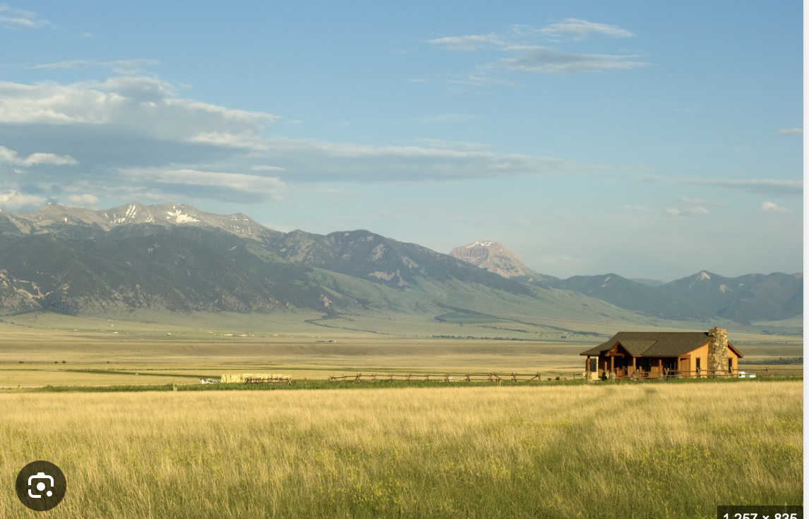 Ranch house on open grassland beneath mountains